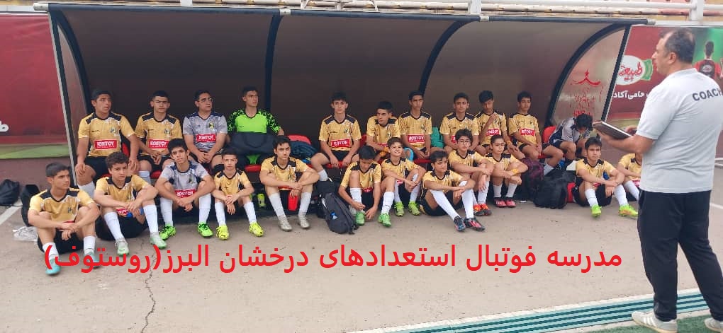 Alt Text عکس گروهی از یک تیم فوتبال جوانان در کرج، شامل 14 بازیکن با لباس‌های زرد و مشکی با لوگوی "Rosto"، نشسته زیر سایه‌بان زمین ورزشی، در کنار یک مربی با لباس خاکستری و نشان "Coach"، در حال دریافت آموزش