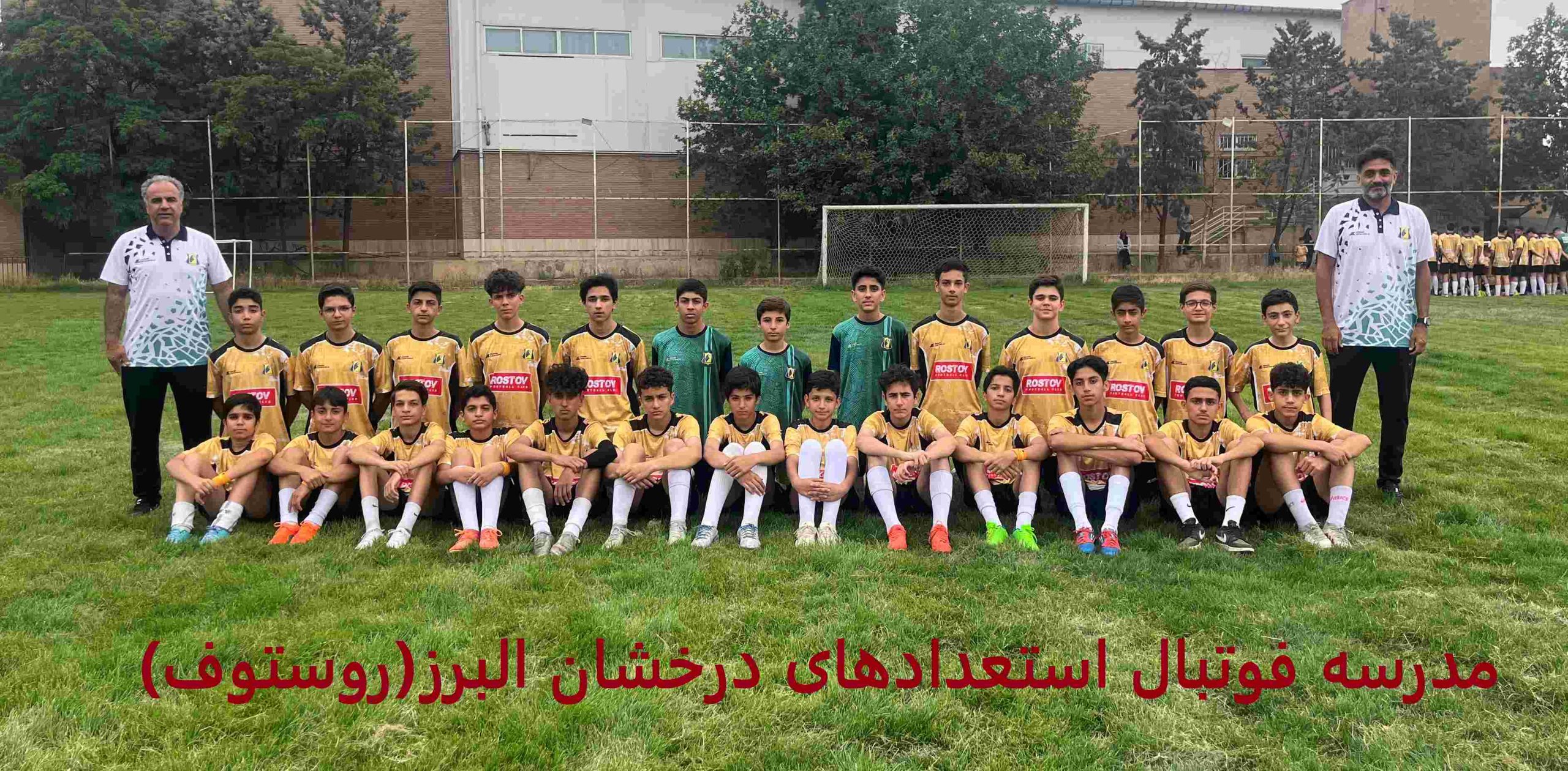 عکس گروهی از تیم فوتبال نوجوانان در کرج، با 16 بازیکن در لباس زرد و مشکی با لوگوی "rostov"، ایستاده و نشسته روی زمین چمن، همراه دو مربی با لباس سفید، با متن "مدرسه فوتبال استعدادهای درخشان" در بالا، نمایش‌دهنده آموزش حرفه‌ای و روحیه تیمی.